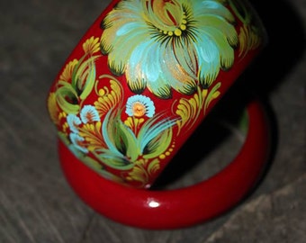 May include: Two red wooden bangles with intricate floral designs painted in green, blue, and yellow. The bangles are stacked on top of each other.
