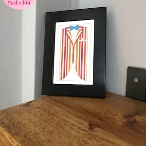 May include: A framed print featuring a colorful illustration of a striped suit jacket with a blue bow tie and pocket square. The frame is black, and the print is displayed on a wooden surface. The text "Digital Download Print n Fold" is in the upper left corner.
