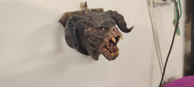 May include: A brown and black monster head sculpture with large horns and an open mouth, mounted on a wall.