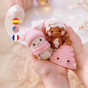 Puede incluir: Tres adornos navideños de crochet: un hombre de jengibre, un muñeco de nieve y un árbol de Navidad rosa. El hombre de jengibre es marrón con glaseado blanco y una cara rosa. El muñeco de nieve es blanco con un sombrero y una bufanda rosas. El árbol de Navidad es rosa con detalles de perlas blancas.