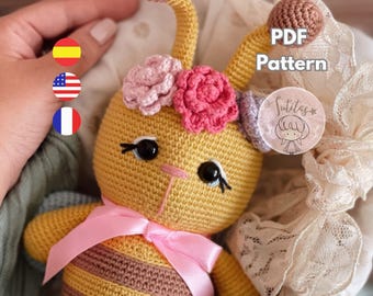 May include: A handmade crochet bee toy with a yellow body and brown stripes. The bee has black eyes, a pink bow, and a floral headband. The image includes the text "PDF Pattern" and a logo.