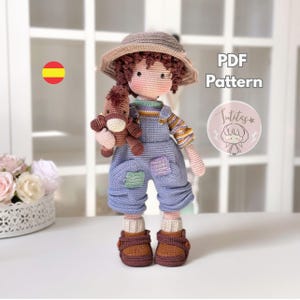 Könnte beinhalten: Eine gehäkelte Puppe mit grauem Hut, gestreiftem Langarmshirt und blauer Latzhose mit Flicken. Die Puppe hält ein kleines braunes gehäkeltes Pferd und trägt braune Schuhe. Der Text auf dem Bild lautet PDF Pattern und Sutitas.