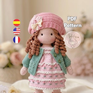Puede incluir: Una muñeca de ganchillo con una boina rosa con flores, una chaqueta verde claro con dos botones y un vestido rosa con volantes blancos y detalles florales. El texto PDF Pattern y Sutitas es visible en el lado derecho.