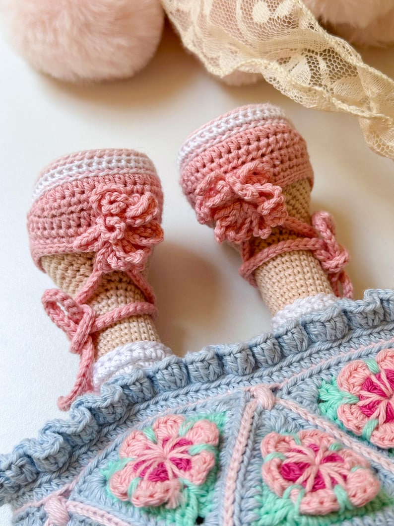 K&ouml;nnte beinhalten: Eine geh&auml;kelte Puppe, die ein blaues Kleid mit rosa Blumen und rosa geh&auml;kelte Schuhe tr&auml;gt.