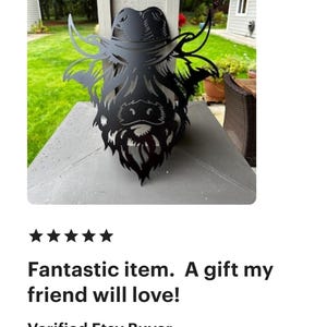 May include: Black metal silhouette of a Highland cow wearing a cowboy hat. The silhouette is mounted on a wooden surface.