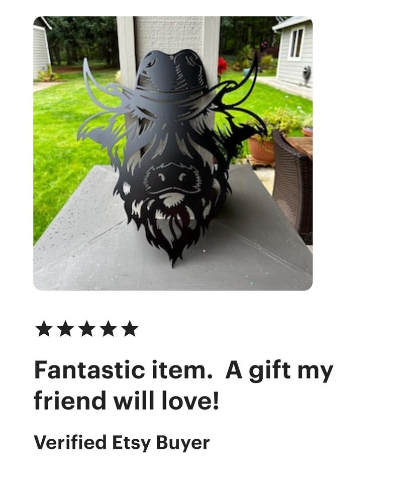 May include: Black metal silhouette of a Highland cow wearing a cowboy hat. The silhouette is mounted on a wooden surface.