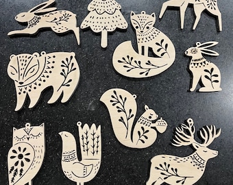 Puede incluir: Un conjunto de 10 adornos de madera con varios animales del bosque y un árbol de Navidad. Los adornos están pintados en blanco y negro con detalles intrincados. Los animales incluyen un ciervo, un zorro, una ardilla, un oso, un conejo, un búho y un pájaro.