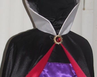 May include: A black satin cape with a white satin collar and red satin lining. The cape has a gold brooch with a red jewel in the center.