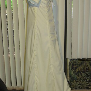 May include: A white, floor-length dress with a fitted bodice and a full skirt. The dress has a lace trim on the sleeves and a lace-up back.