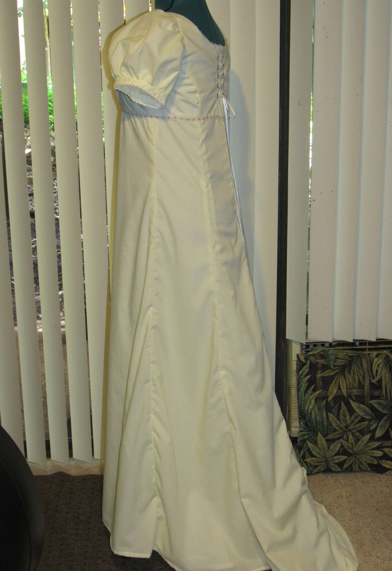 May include: A white, floor-length dress with a fitted bodice and a full skirt. The dress has a lace trim on the sleeves and a lace-up back.