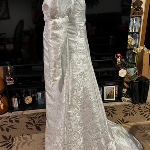 May include: A white, long-sleeved gown with a paisley pattern. The gown has a fitted bodice and a flowing skirt.