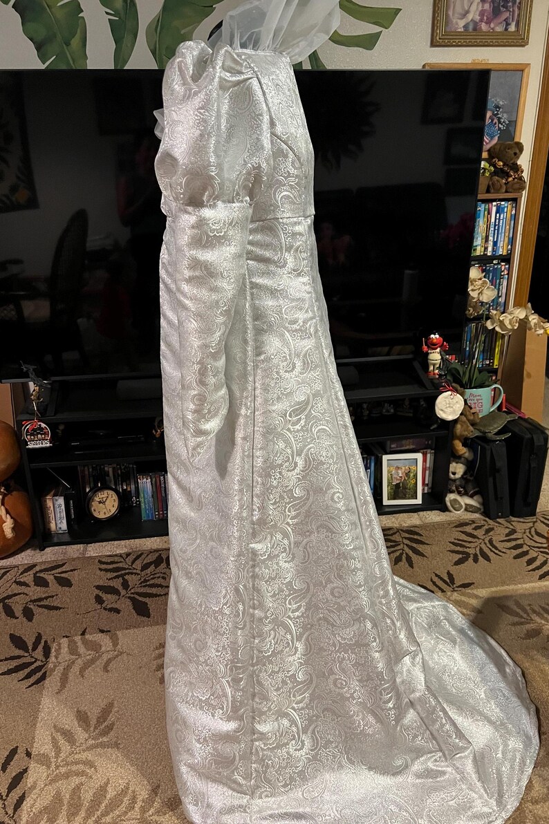 May include: A white, long-sleeved gown with a paisley pattern. The gown has a fitted bodice and a flowing skirt.