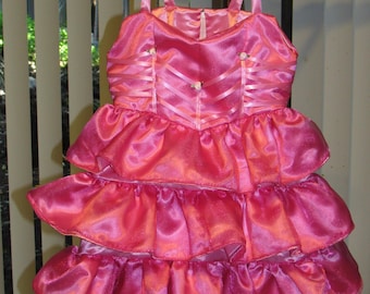 May include: A pink satin dress with multiple layers of ruffles. The dress has a sweetheart neckline and thin straps. The bodice is decorated with satin ribbon and small pearl-like embellishments.