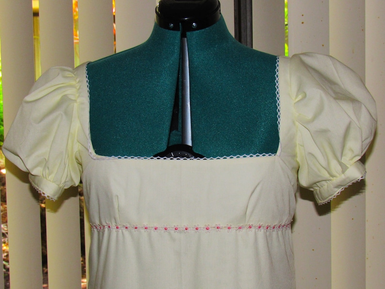 May include: A white dress with puffed sleeves and a square neckline. The dress has a pink trim around the waist.
