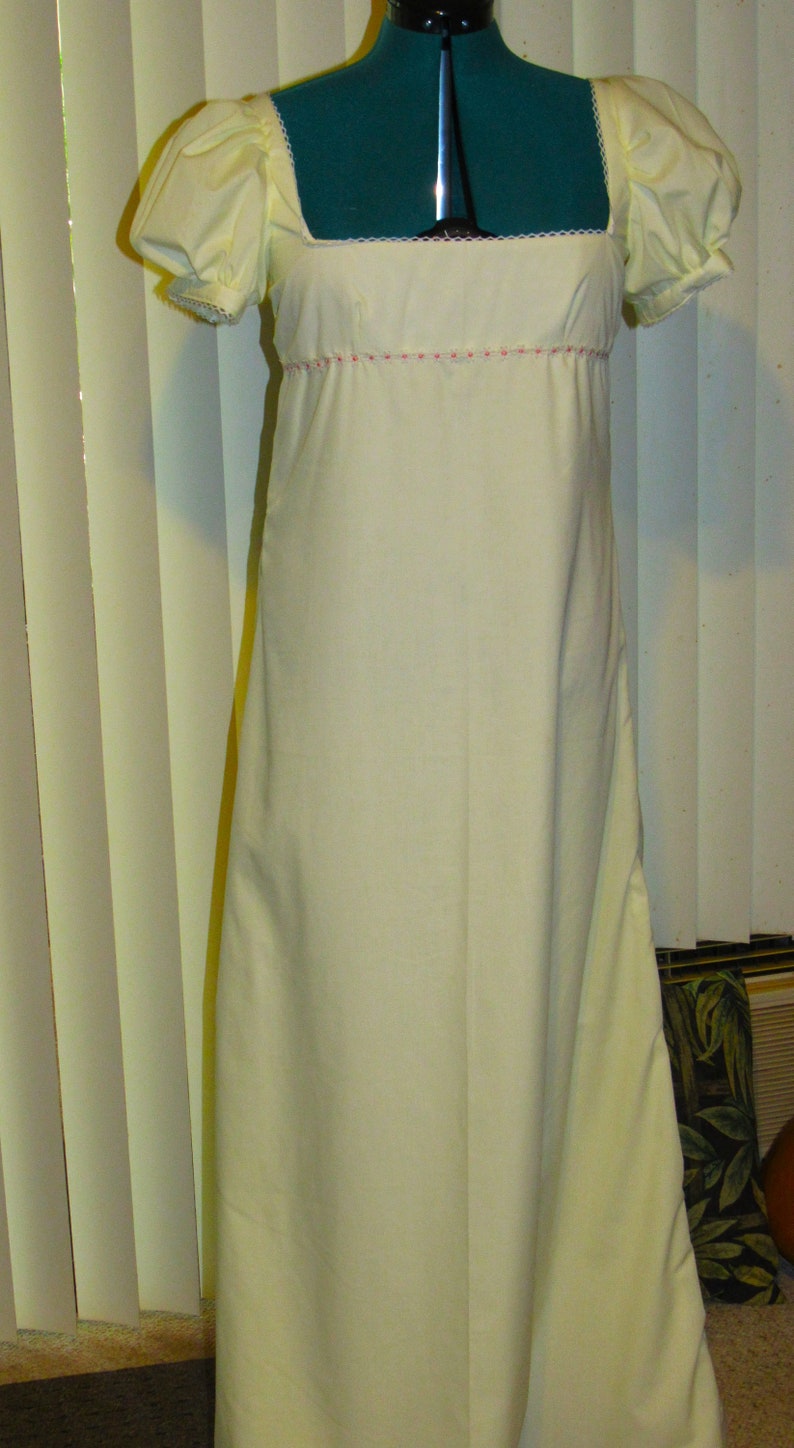 May include: A white, long-sleeved dress with puffed sleeves and a lace trim around the neckline. The dress has a simple, elegant design.