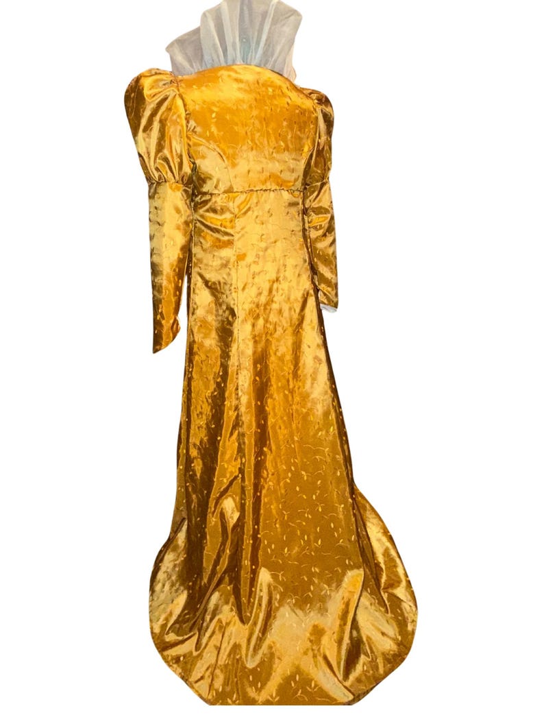 May include: A long, golden yellow gown with a high neckline and puffed sleeves. The gown has a subtle pattern of small dots and is made of a shiny fabric.