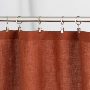 May include: A rust-colored linen shower curtain with silver metal clips hanging on a silver shower rod.