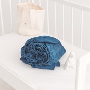 May include: A white crib with a blue fitted sheet and a white bunny-shaped storage basket.