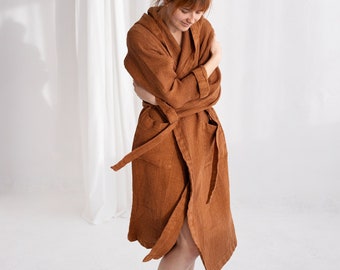 May include: A brown waffle-weave robe with a wrap-around design. The robe has a tie belt and is knee-length. The fabric appears soft and comfortable. The background is a plain white wall and a white curtain.