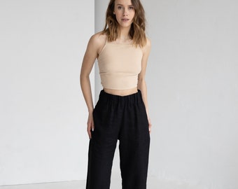 May include: A woman wearing a beige ribbed tank top and black linen pants. The pants have a wide-leg design. The outfit is simple and casual, suitable for everyday wear.