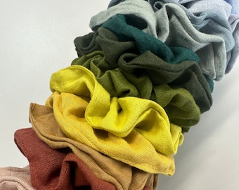 Puede incluir: Una pila de scrunchies de tela coloridos en tonos de azul, verde, amarillo, naranja y marrón. Los scrunchies están hechos de una tela suave y texturizada y son perfectos para agregar un toque de color a cualquier atuendo.
