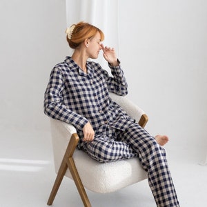 May include: A woman wearing a blue and white gingham pajama set sits in a white armchair with a brown woven rug on the floor.