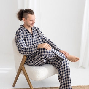 Könnte beinhalten: Eine Person in einem blau-weiß karierten Schlafanzug sitzt auf einem weißen Stuhl mit Holzbeinen. Der Stuhl steht auf einem braunen gewebten Teppich.