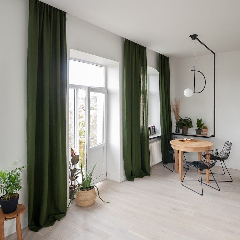 May include: A dining room with a wooden table and four black metal chairs. The room has large windows with green curtains and a modern light fixture hanging from the ceiling.