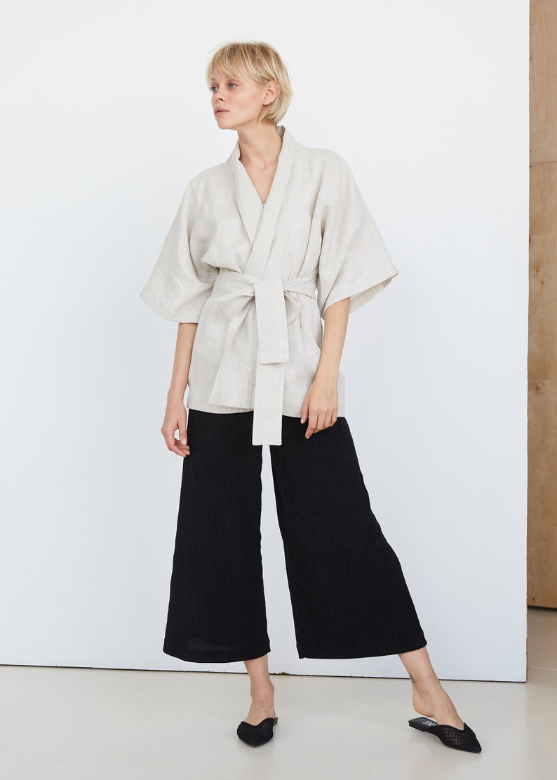 Może przedstawiać: Jasza w kolorze jasnobeżowym wykonana z lnu z paskiem do wiązania. Kimono ma luźny kr&oacute;j i rękaw &frac34;. Modelka ma na sobie czarne szerokie spodnie i czarne baleriny.
