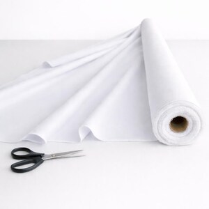 May include: A roll of solid white fabric partially unrolled to reveal a smooth, opaque texture. Beside the fabric roll lies a pair of black metal scissors with a pointed tip and ergonomic handles, ready for cutting the textile material.