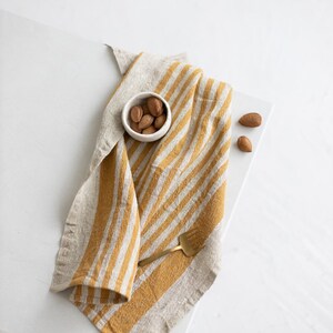May include: A yellow and white striped linen kitchen towel with a small white bowl of almonds and a gold fork on top.