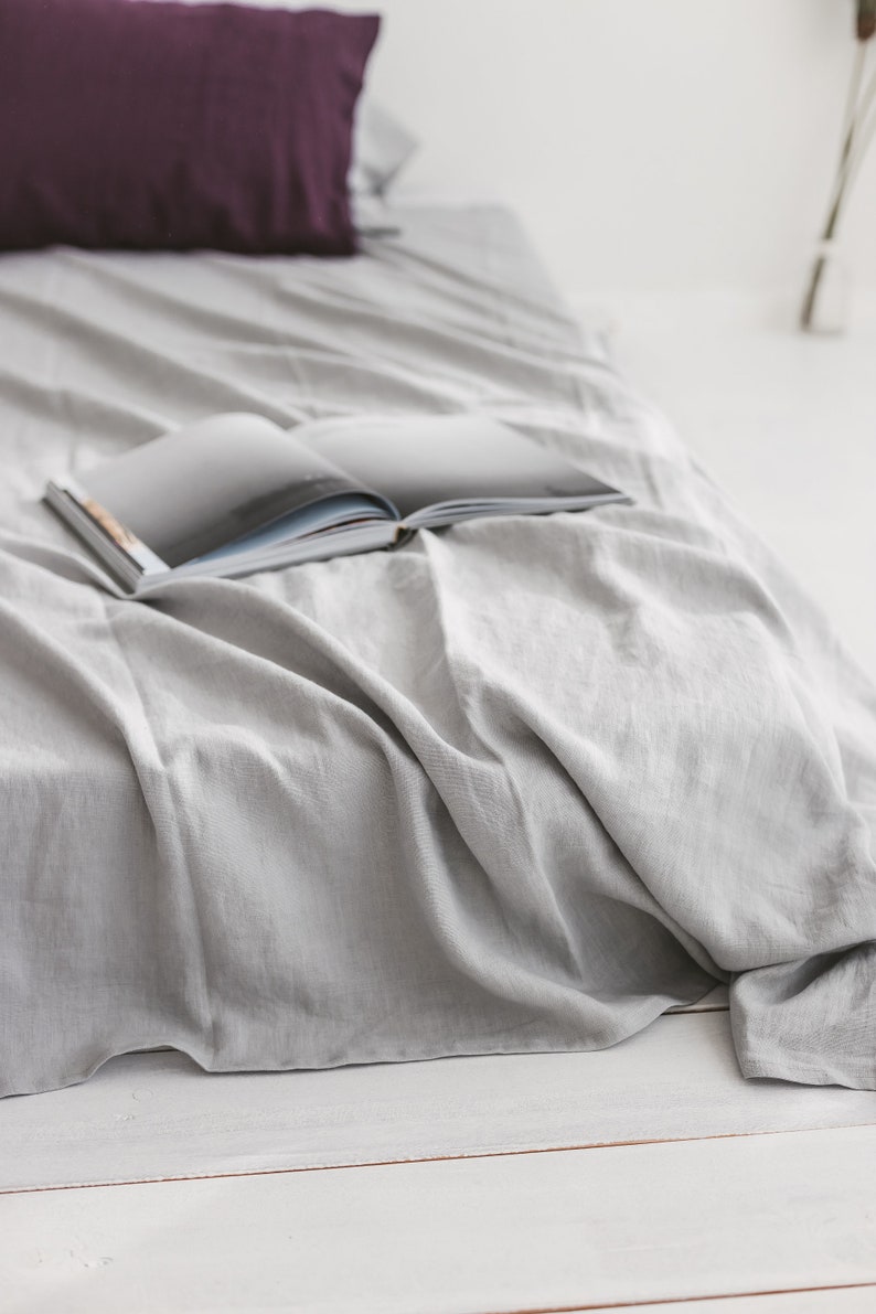 Peut inclure: Un couvre-lit en lin gris avec un livre ouvert dessus. Le livre est ferm&eacute; et a une couverture blanche.