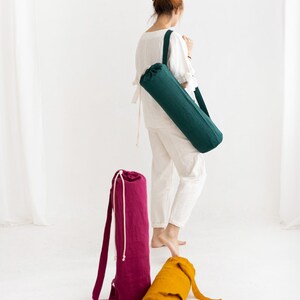 Puede incluir: Tres bolsas para esterillas de yoga en diferentes colores: verde, rosa y amarillo. Las bolsas est&aacute;n hechas de tela y tienen un cierre de cord&oacute;n. Las bolsas est&aacute;n sobre una superficie blanca.