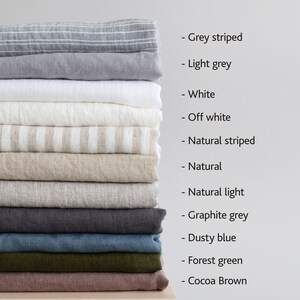 Op de afbeelding: Een stapel van 12 linnen stofstalen in verschillende kleuren en patronen, waaronder grijs gestreept, lichtgrijs, wit, off white, naturel gestreept, naturel, naturel licht, grafietgrijs, stofig blauw, bosgroen en cacao bruin.