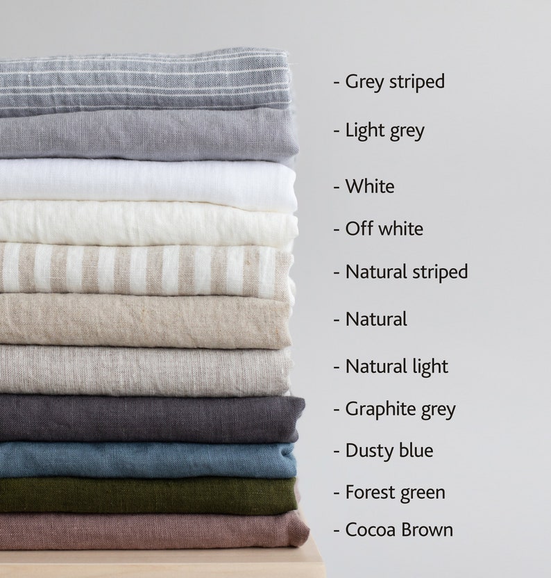 Op de afbeelding: Een stapel van 12 linnen stofstalen in verschillende kleuren en patronen, waaronder grijs gestreept, lichtgrijs, wit, off white, naturel gestreept, naturel, naturel licht, grafietgrijs, stofig blauw, bosgroen en cacao bruin.