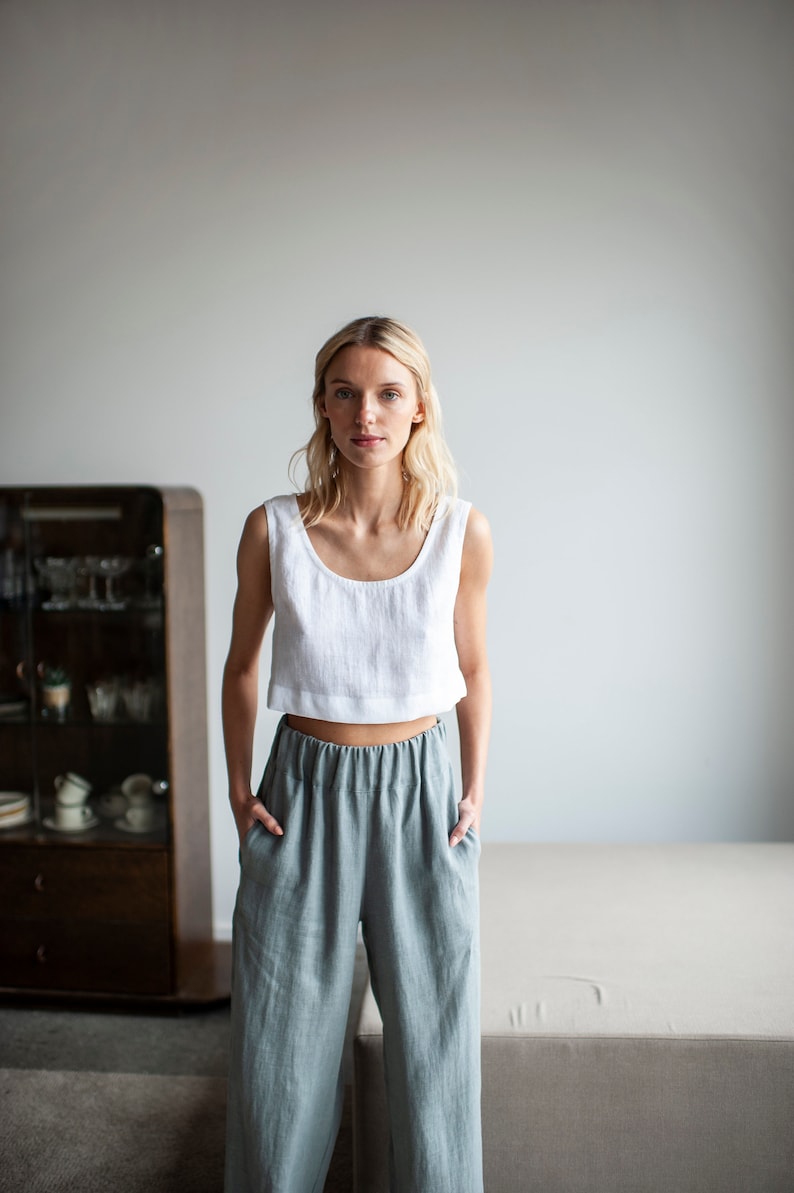 K&ouml;nnte beinhalten: Eine Frau tr&auml;gt ein wei&szlig;es Leinen-Crop-Top und eine Hose aus salbeigr&uuml;nem Leinen. Das Top hat einen Rundhalsausschnitt. Die Hose ist hoch tailliert, weit geschnitten und hat einen elastischen Bund. Das Outfit ist l&auml;ssig.