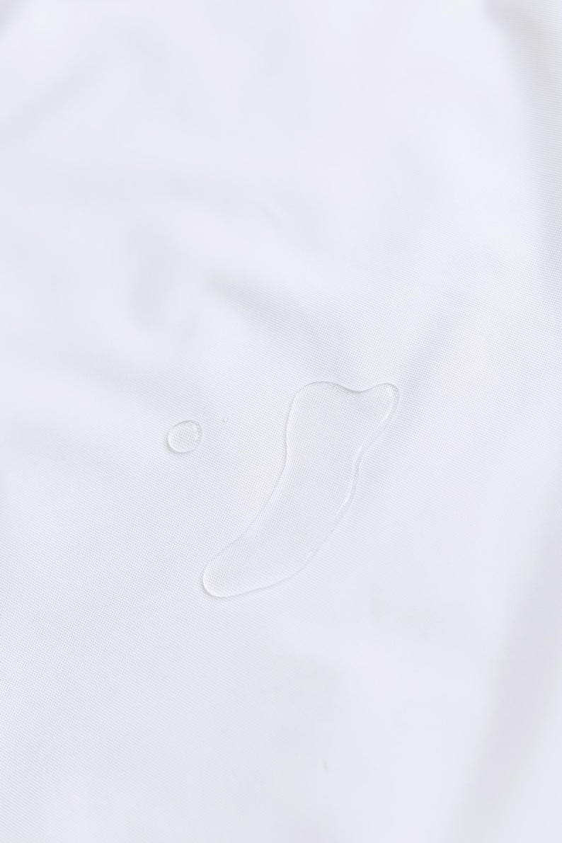 May include: Close-up of a white fabric with two water droplets. One droplet is small and round, while the other is a larger, elongated shape. The fabric has a subtle texture.