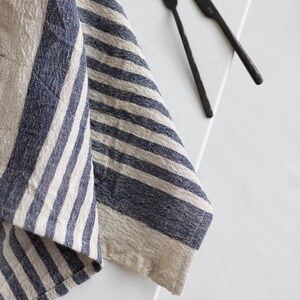 May include: A blue and white striped linen kitchen towel folded on a white surface with two black metal utensils, a fork and a knife.