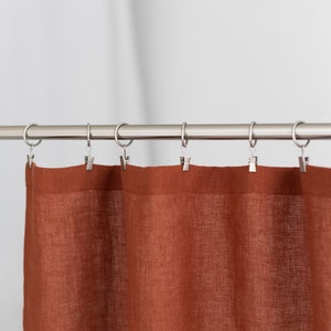 May include: A rust-colored linen curtain hangs from a silver curtain rod with silver clips.