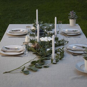 Pu&ograve; includere: Una tavola apparecchiata con candele bianche, piatti bianchi e una ghirlanda verde. La tavola &egrave; apparecchiata per una cena con tovaglioli bianchi e posate.