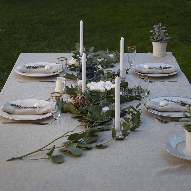 Pu&ograve; includere: Una tavola apparecchiata con candele bianche, piatti bianchi e una ghirlanda verde. La tavola &egrave; apparecchiata per una cena con tovaglioli bianchi e posate.