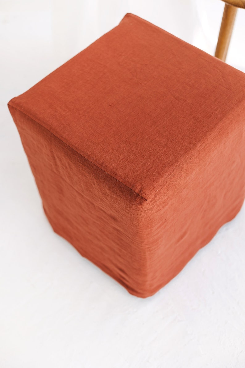May include: A square, terracotta-coloured linen ottoman with a smooth, textured surface.