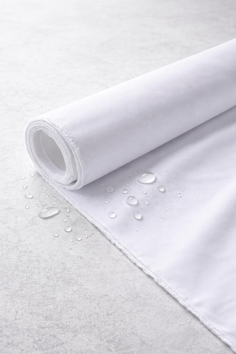 May include: A roll of white fabric with a textured surface, partially unrolled to reveal the inner layers. Water droplets are scattered across the fabric, suggesting a waterproof or water-resistant quality. The fabric's edge is visible.