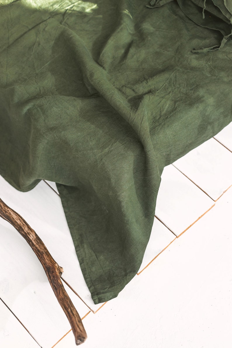 Peut inclure: Un tissu en lin vert fonc&eacute; drap&eacute; sur une surface blanche. Le tissu est froiss&eacute; et a une texture naturelle.