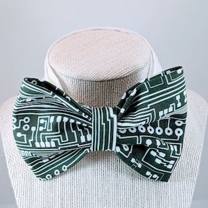 Könnte beinhalten: Eine grüne Fliege mit einem weißen Schaltkreis-Muster. Die Fliege wird auf einer weißen Puppe präsentiert.