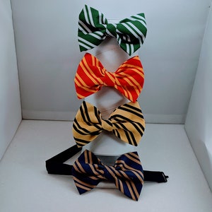 May include: Four bow ties with different colored stripes. The bow ties are displayed on a white stand. The bow ties are green and white, red and yellow, yellow and black, and blue and gold.