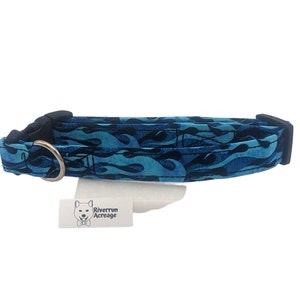 May include: Blue and black dog collar with a flame pattern. The collar has a black buckle and a silver D-ring. The collar is made by Riverrun Acreage.