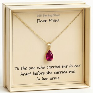 May include: A gold-colored necklace with a teardrop-shaped, deep pink gemstone pendant. The necklace is displayed in a cream-colored box with the text "925 Sterling Silver Dear Mom" and a sentimental quote.