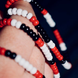 May include: A close-up of a multi-coloured beaded bracelet with red, white and black beads. The bracelet is wrapped around a person's wrist.