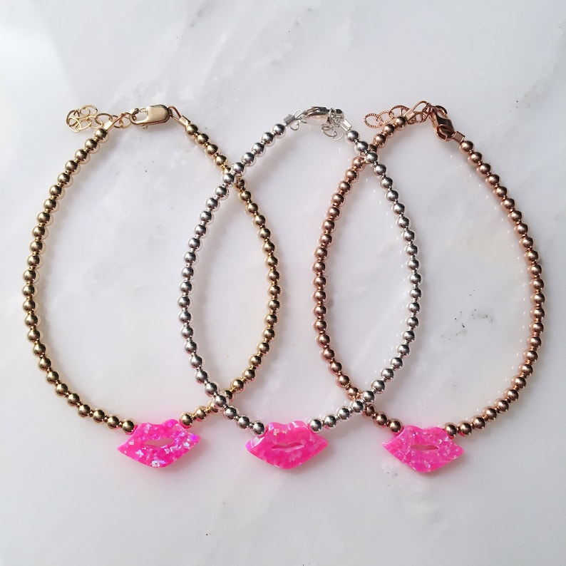 Puede incluir: Tres delicados brazaletes de cuentas con un dije de labios de &oacute;palo rosa. Los brazaletes est&aacute;n disponibles en oro, plata y oro rosa.